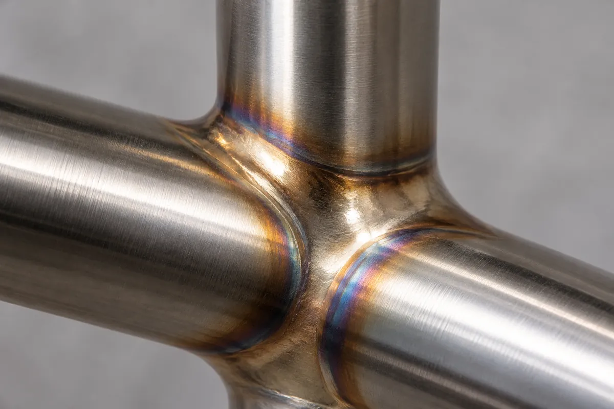 macro of a smooth filler-metal fillet at a stainless tube junction beside a distinct fusion-welded joint.