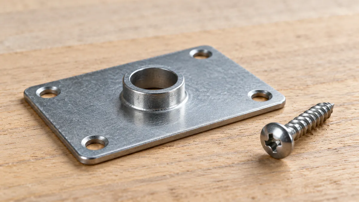 Macro of a thin steel mounting plate with a short raised extruded hole collar, nearby separate screw, no invented cutaway