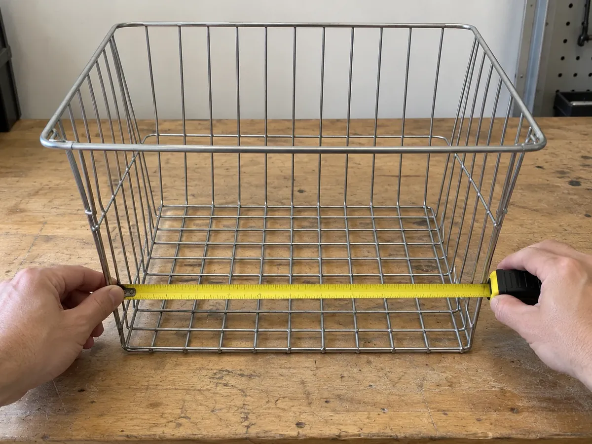 Buyer measuring clear inside width of a tapered wire closet basket near its lower section